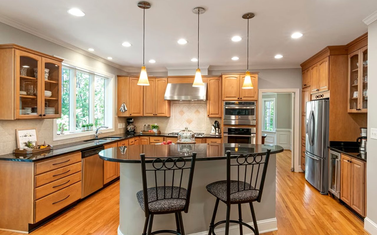 Kitchen with warm wood cabinets, stainless steel appliances, and a large curved island with two bar stools.