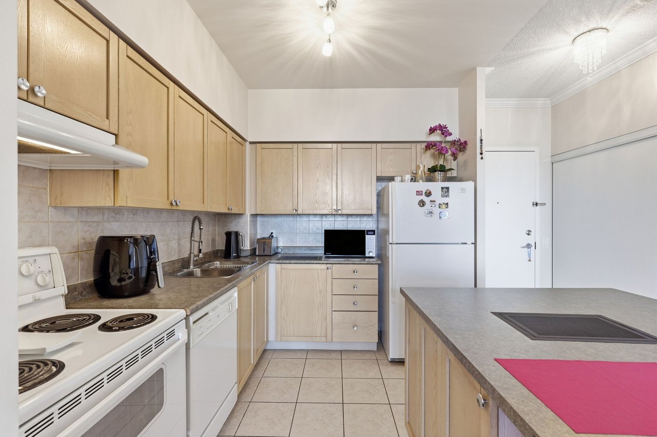 Condo kitchen with light wood cabinets, tiled floors, and a large island cooktop.