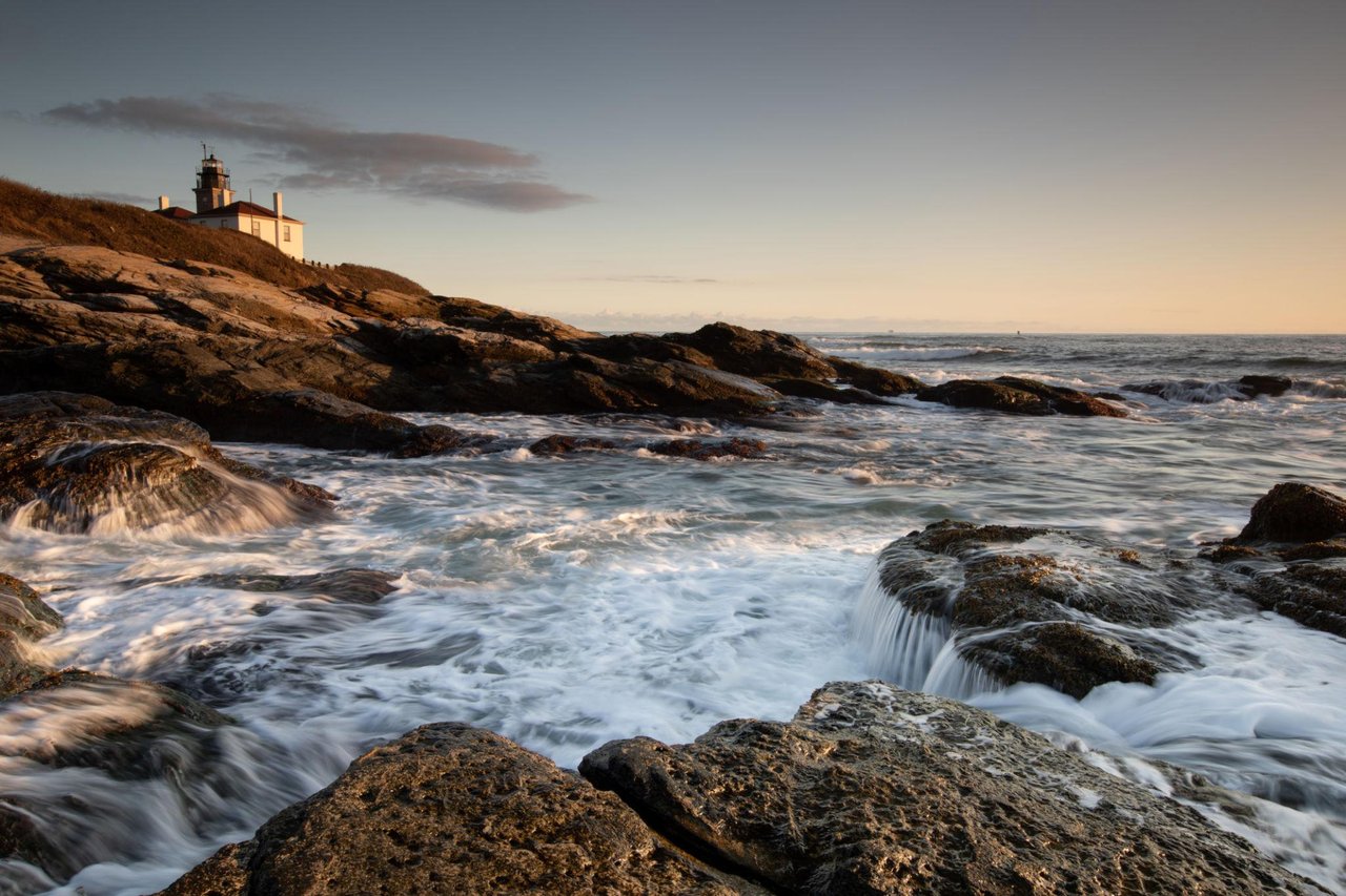 Lighthouse on a rocky point above foaming ocean waves at golden hour.