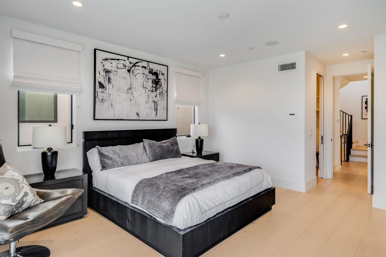 Furnished bedroom with a black bed, gray throw, abstract wall art, and light wood floors.