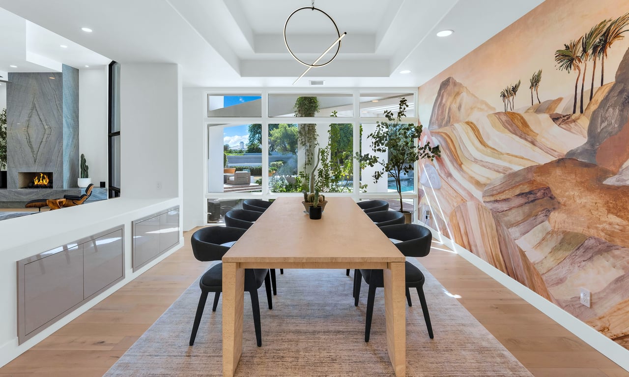 Dining room with a long wood table, desert mural, fireplace, and windows overlooking the pool.