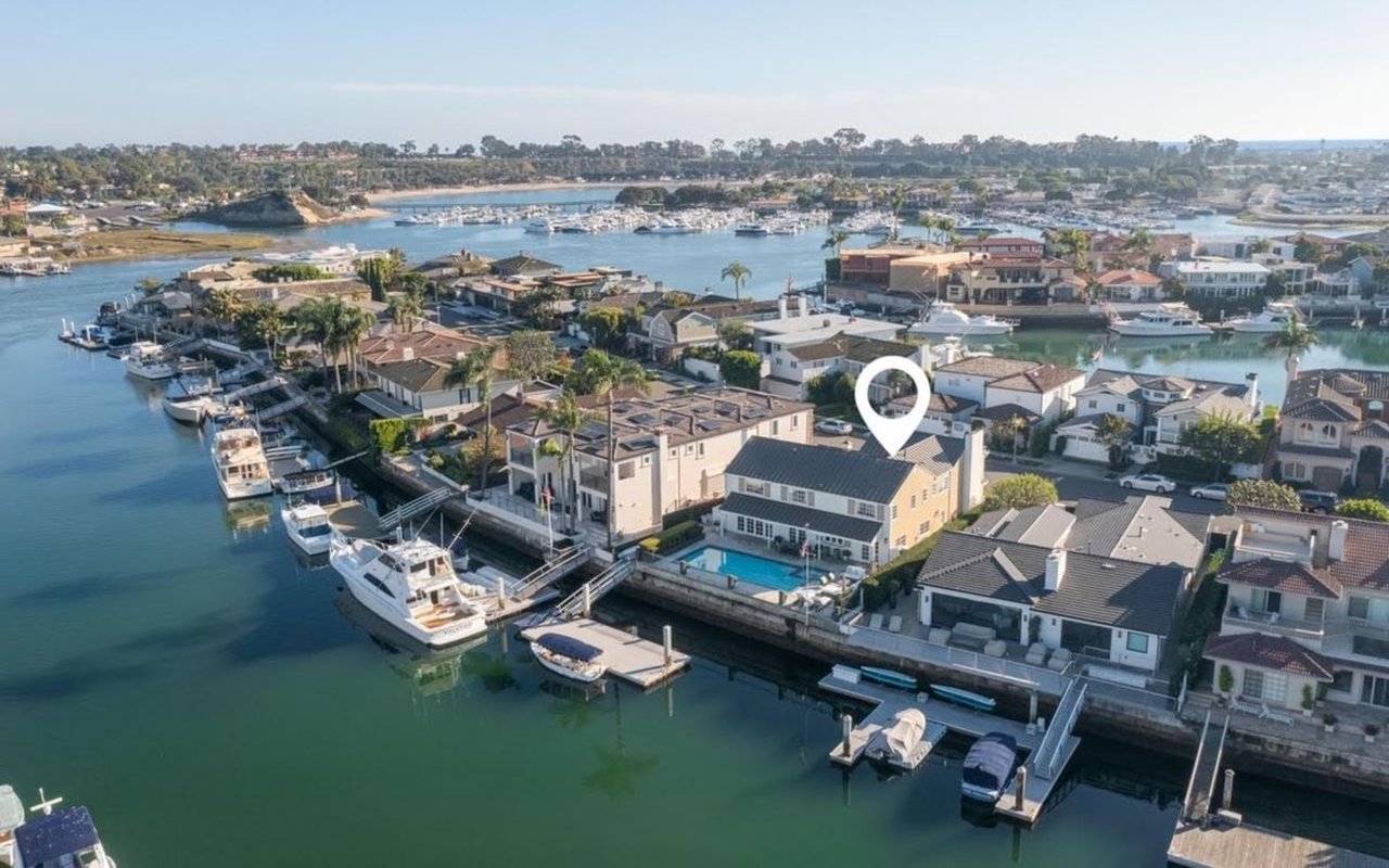  An aerial view of a coastal neighborhood with a large white pin marking a house with a pool and a dock on the water.