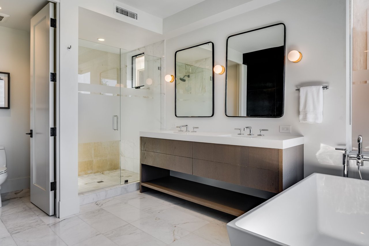 Modern bathroom with a glass walk-in shower, double vanity, marble floors, and freestanding tub.