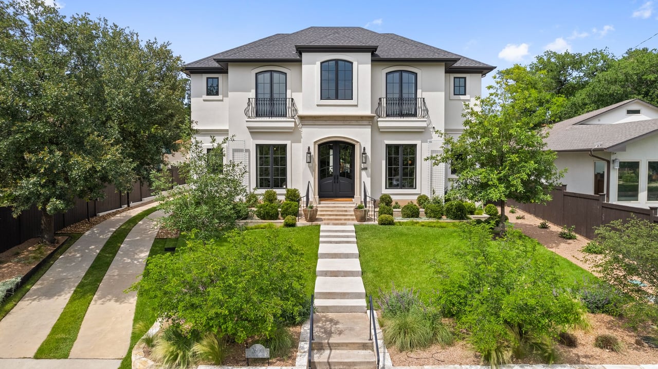 Front elevation of a two-story stucco home with an arched entry and mature oak trees at 2600 Westover Road in Tarrytown, Austin, built by Trey Smith Builders.