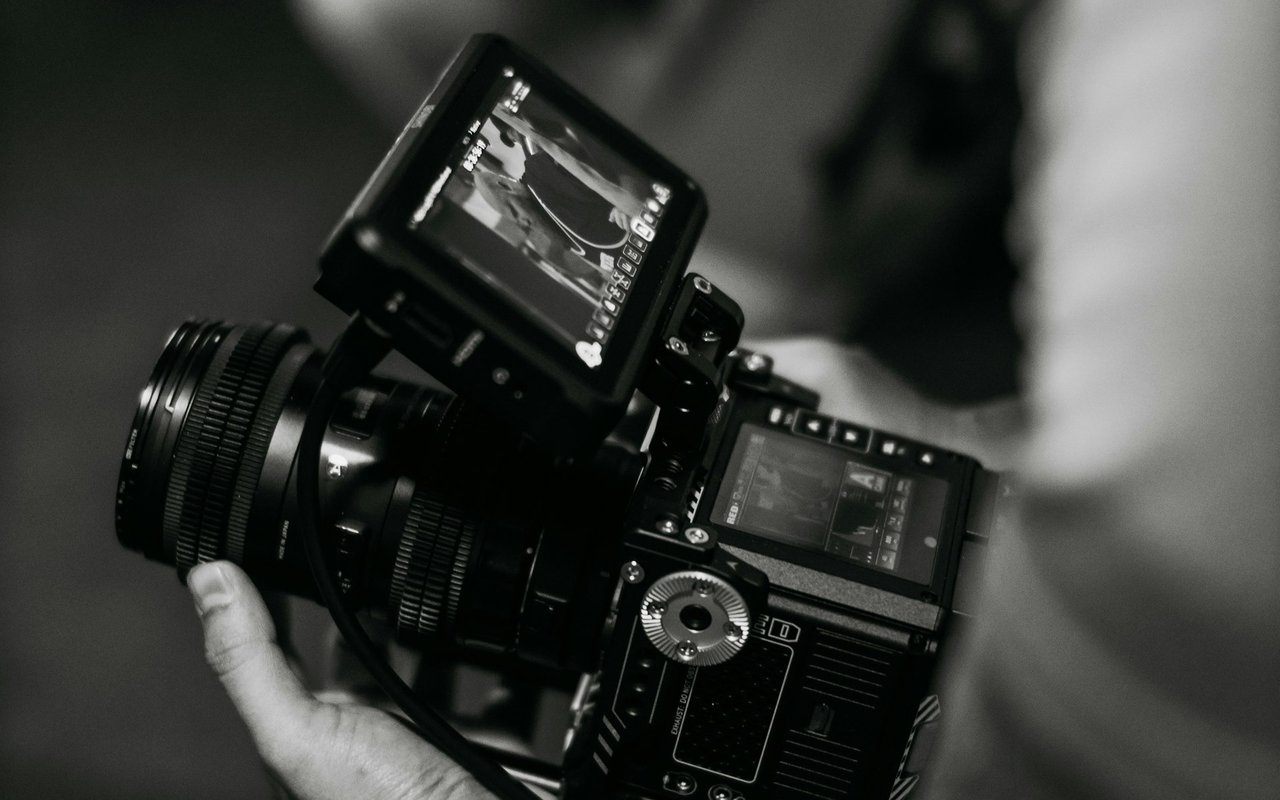 Professional video camera with a top-mounted monitor, supported by a hand.