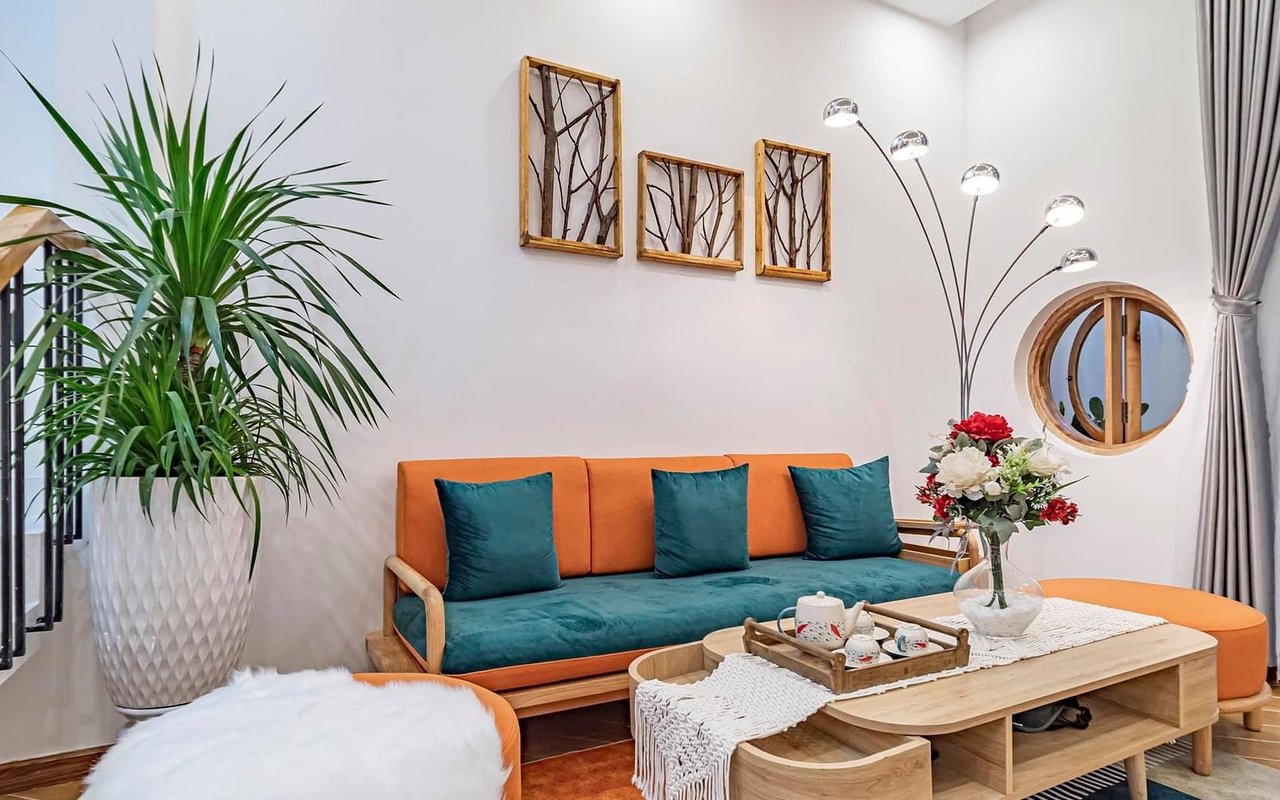 Living room with an orange-and-teal sofa, wood coffee table, tall potted plant, and round window.