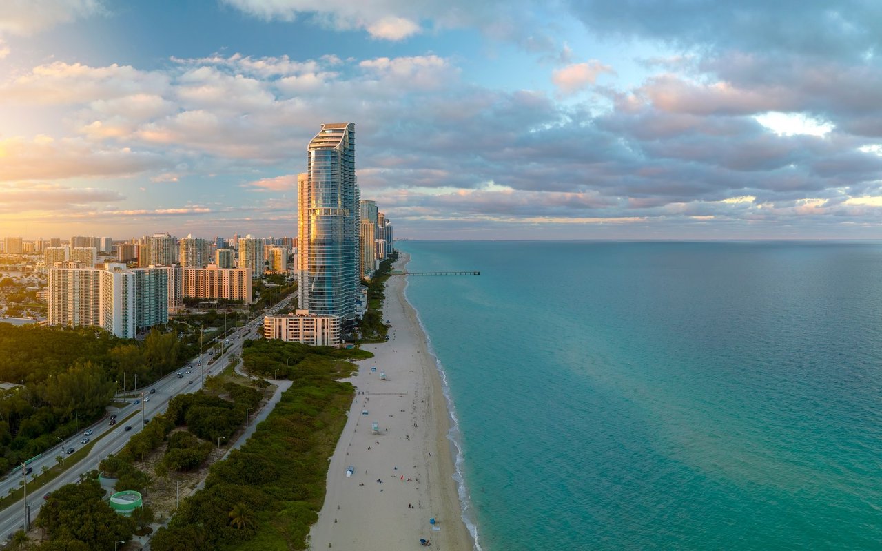 Aerial view of beachfront towers and city skyline beside turquoise water at golden hour.