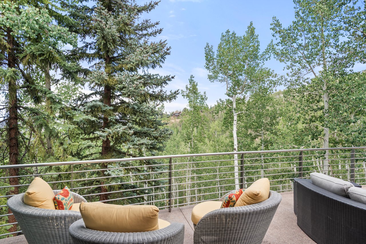 Outdoor deck with wicker seating and a metal railing overlooking a wooded hillside.
