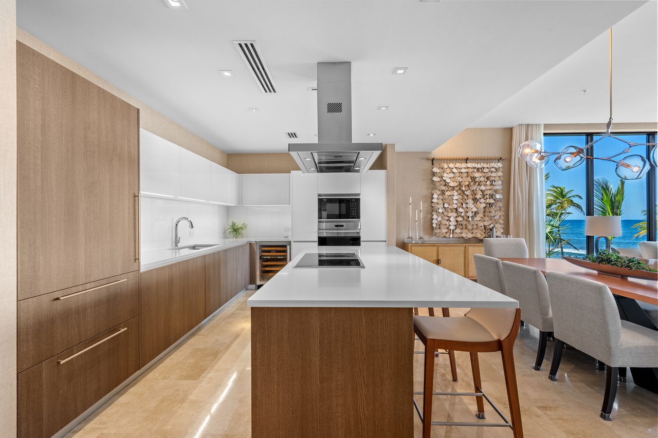 Modern kitchen with wood cabinetry and a large island, opening to an ocean-view dining area.