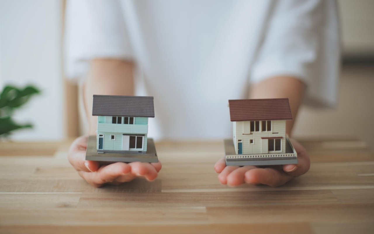 Hands holding two miniature houses side by side