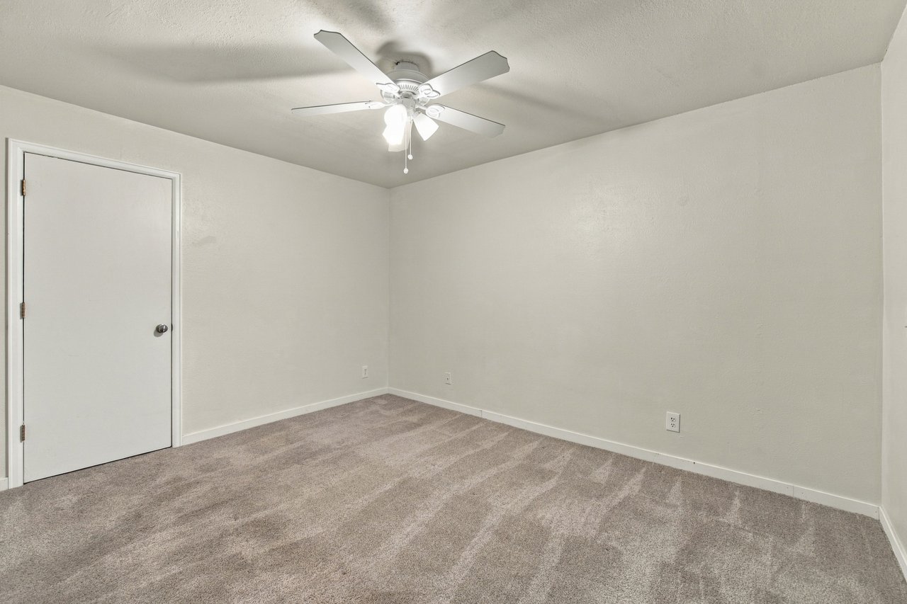 Empty carpeted bedroom with a ceiling fan and light.