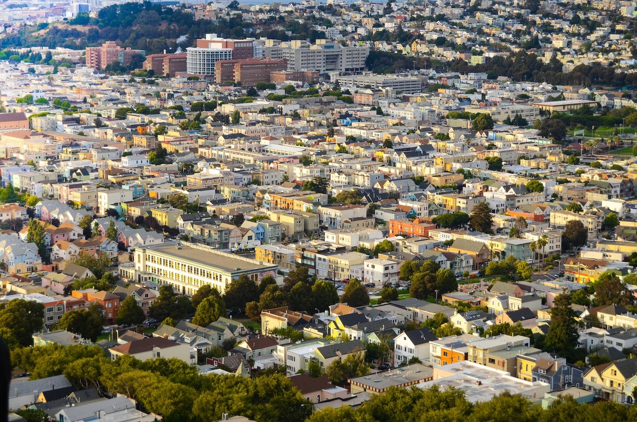 Aerial view of San Francisco’s Mission District with colorful buildings, tree-lined streets, and city skyline in the distance