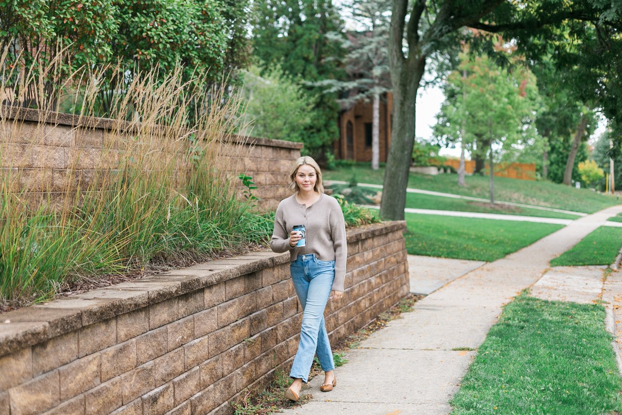 Cait Berry, a local Madison real estate expert with Insiders Realty, walking through a Dane County neighborhood holding a coffee cup, ready to help buyers and sellers navigate the spring market.