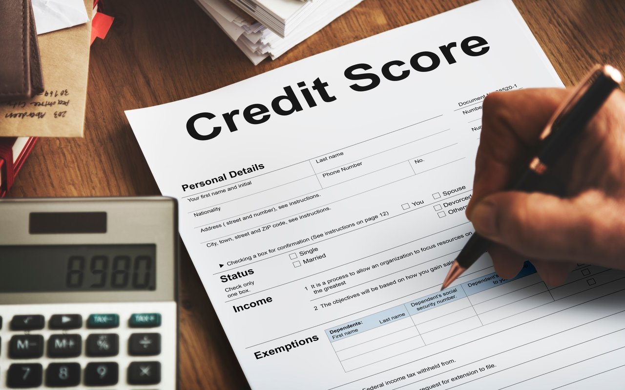A hand fills out a credit score form beside a calculator.