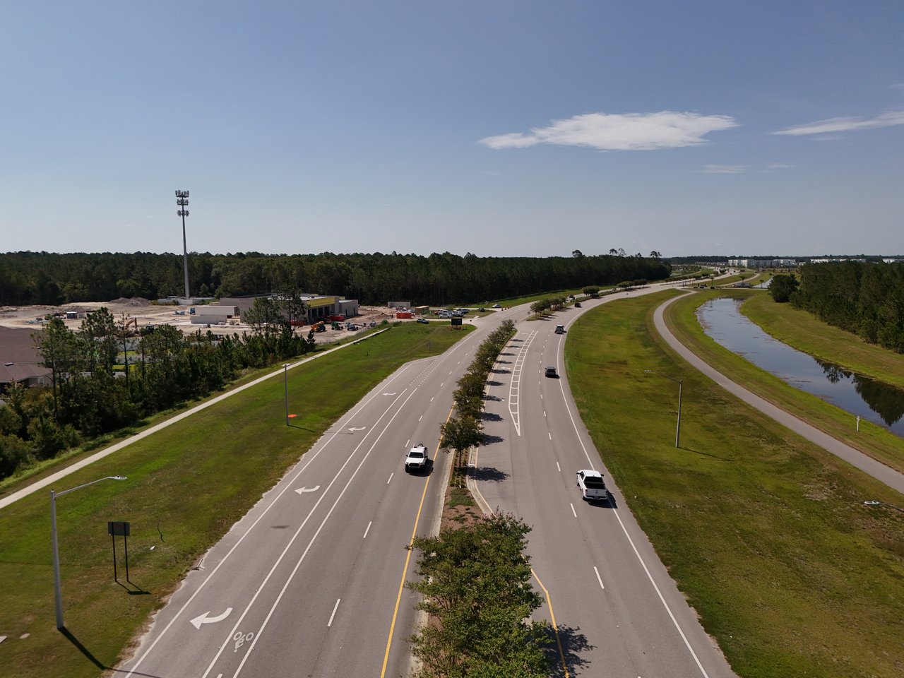 Aerial view of a divided road curving past a construction site and a pond.