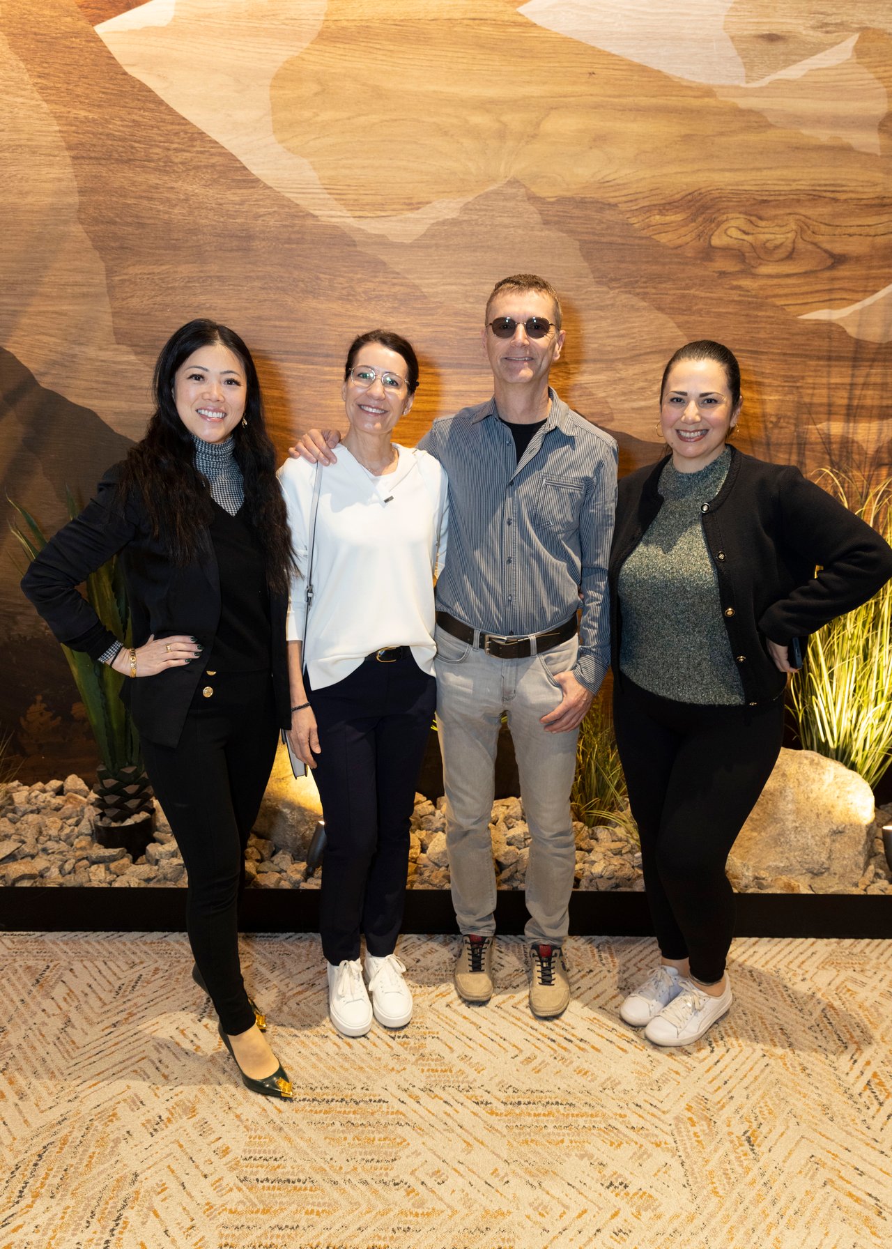 Four adults pose together in front of a wood-patterned wall at an indoor event.