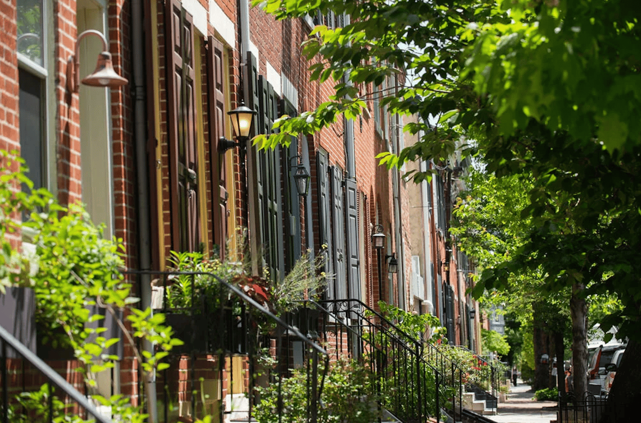 Queen Village street lined with brick rowhouses, stoops, and leafy trees.