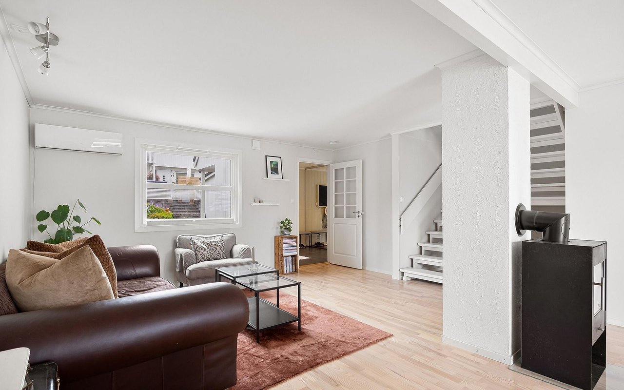 Furnished living room with a dark leather sofa, glass coffee table, staircase, and black wood stove.
