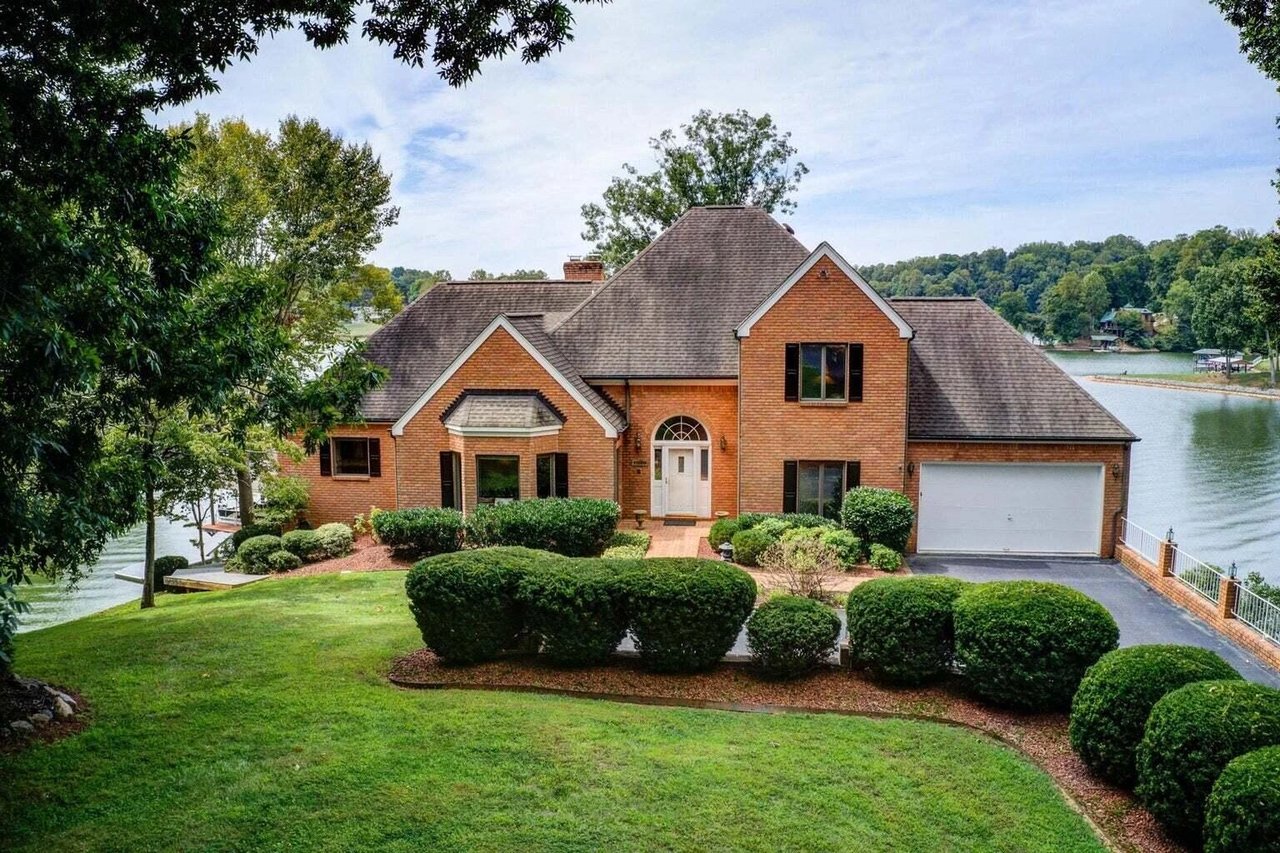 Red-brick lakeside house with a landscaped lawn, steep roof, and attached garage.