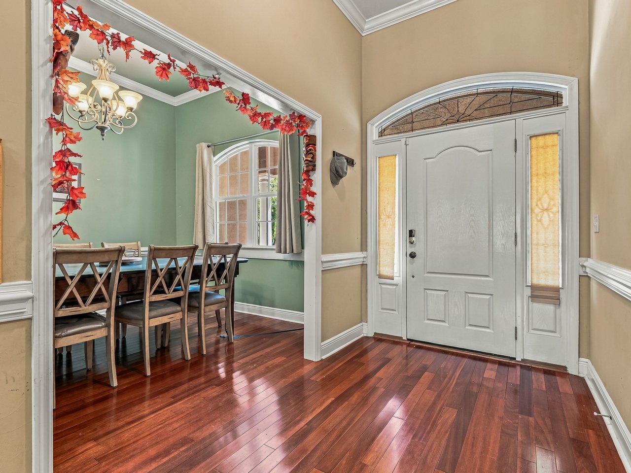Entry foyer with a white front door, hardwood floors, and a dining area framed by autumn leaf garland.