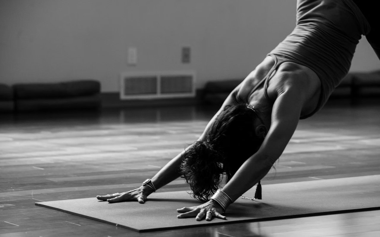 Woman practicing downward-facing dog on a yoga mat indoors.