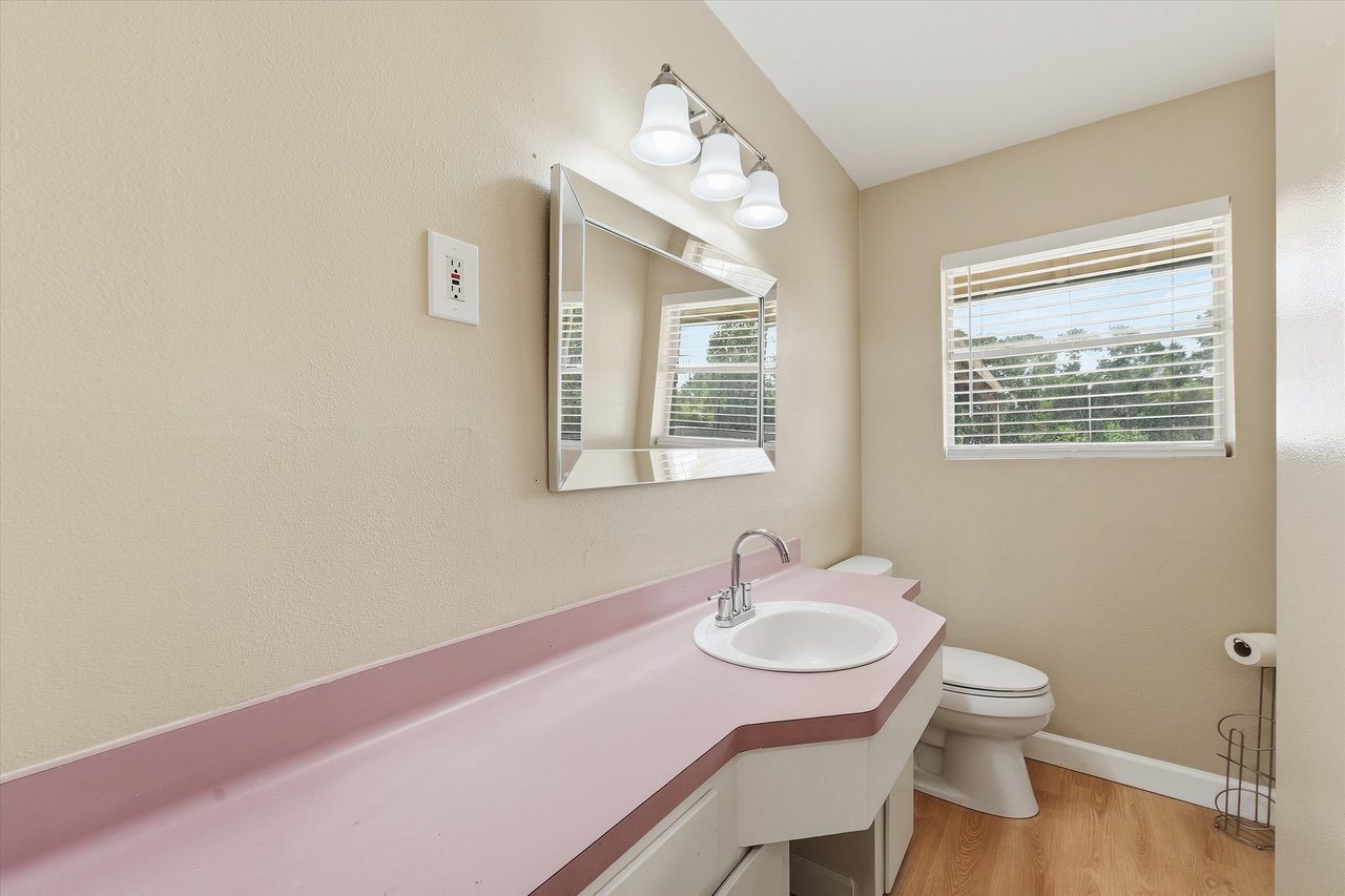 Bathroom with a long pale pink vanity countertop, white sink, and window with blinds.