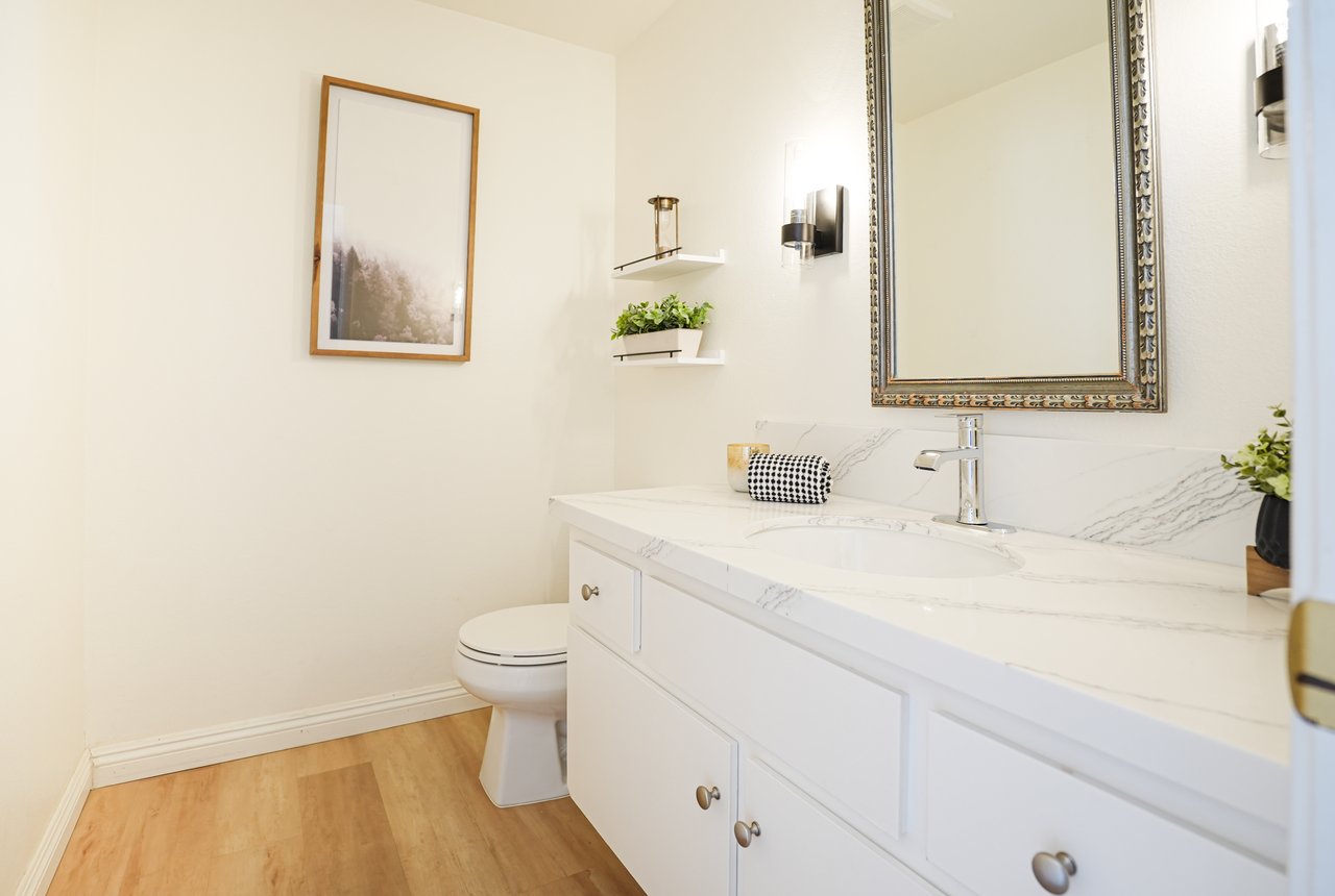 Stylish bathroom at 6321 Caminito Luisito, San Diego CA 92111, featuring a white marble vanity with chrome faucet, framed mirror, floating shelves with greenery, wood-style flooring, and neutral modern design.