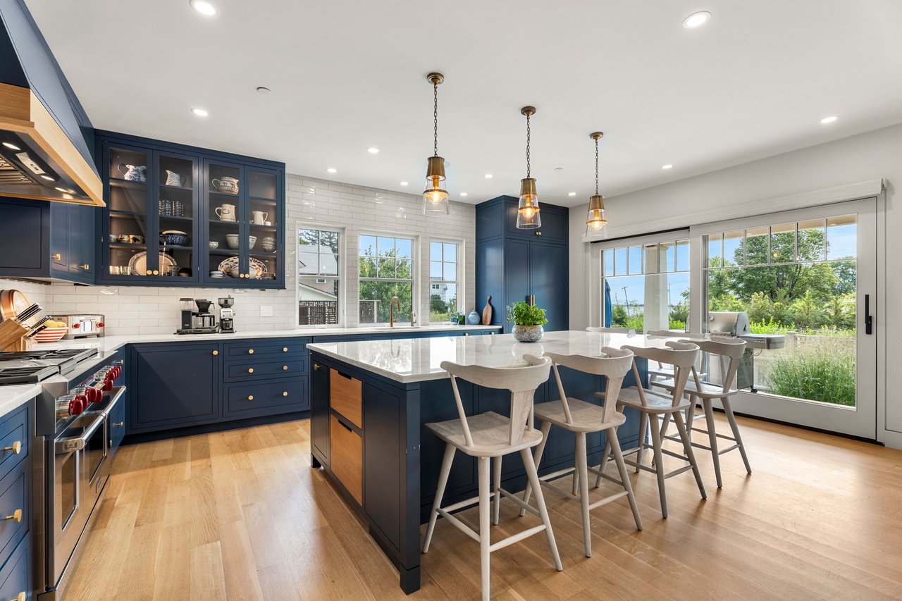Renovated kitchen with navy cabinets, a marble island, bar stools, and sliding glass doors to a garden.