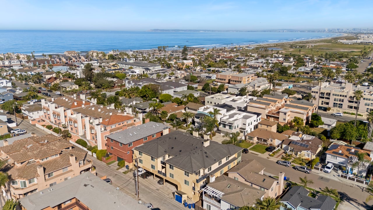 Coastal neighborhood of homes beside a long sandy beach and blue ocean, viewed from above.