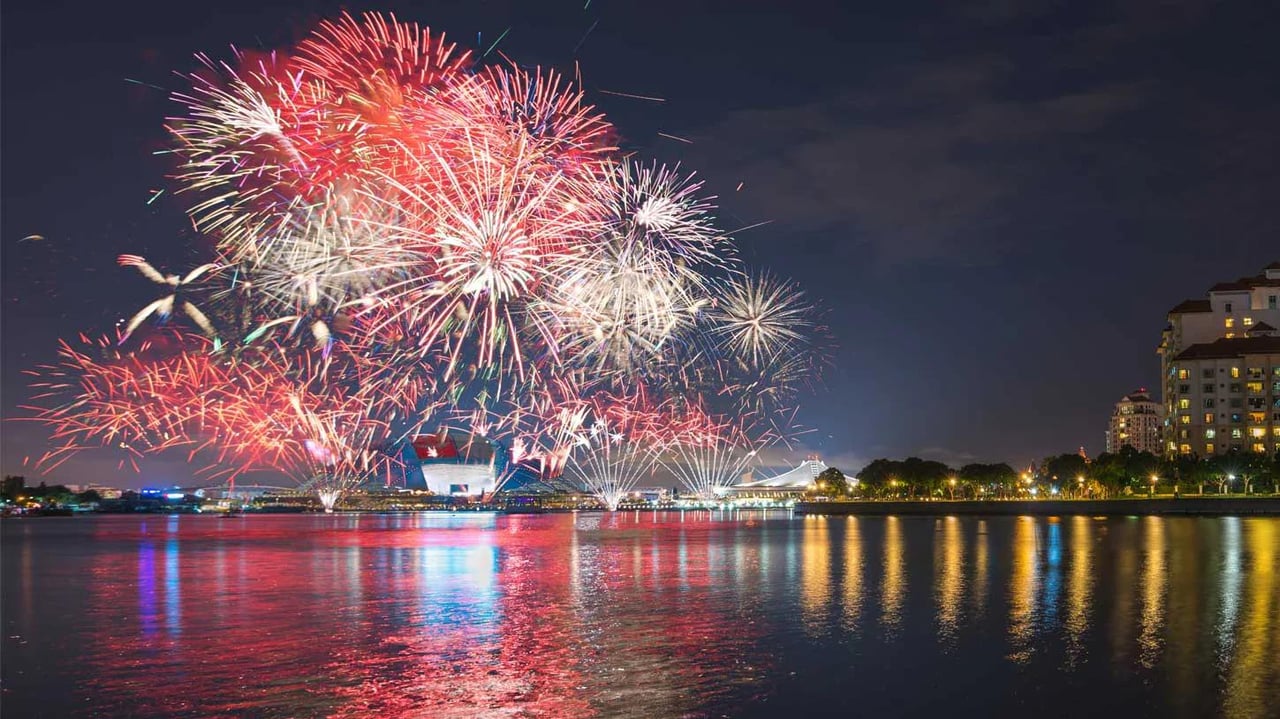 Colorful Independence Day fireworks reflecting over the water during an evening celebration.