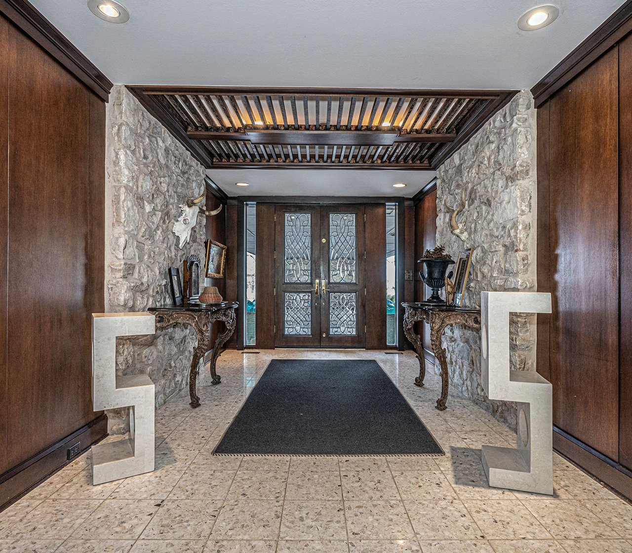 Entry hall with stone walls, carved console tables, and decorative double doors.