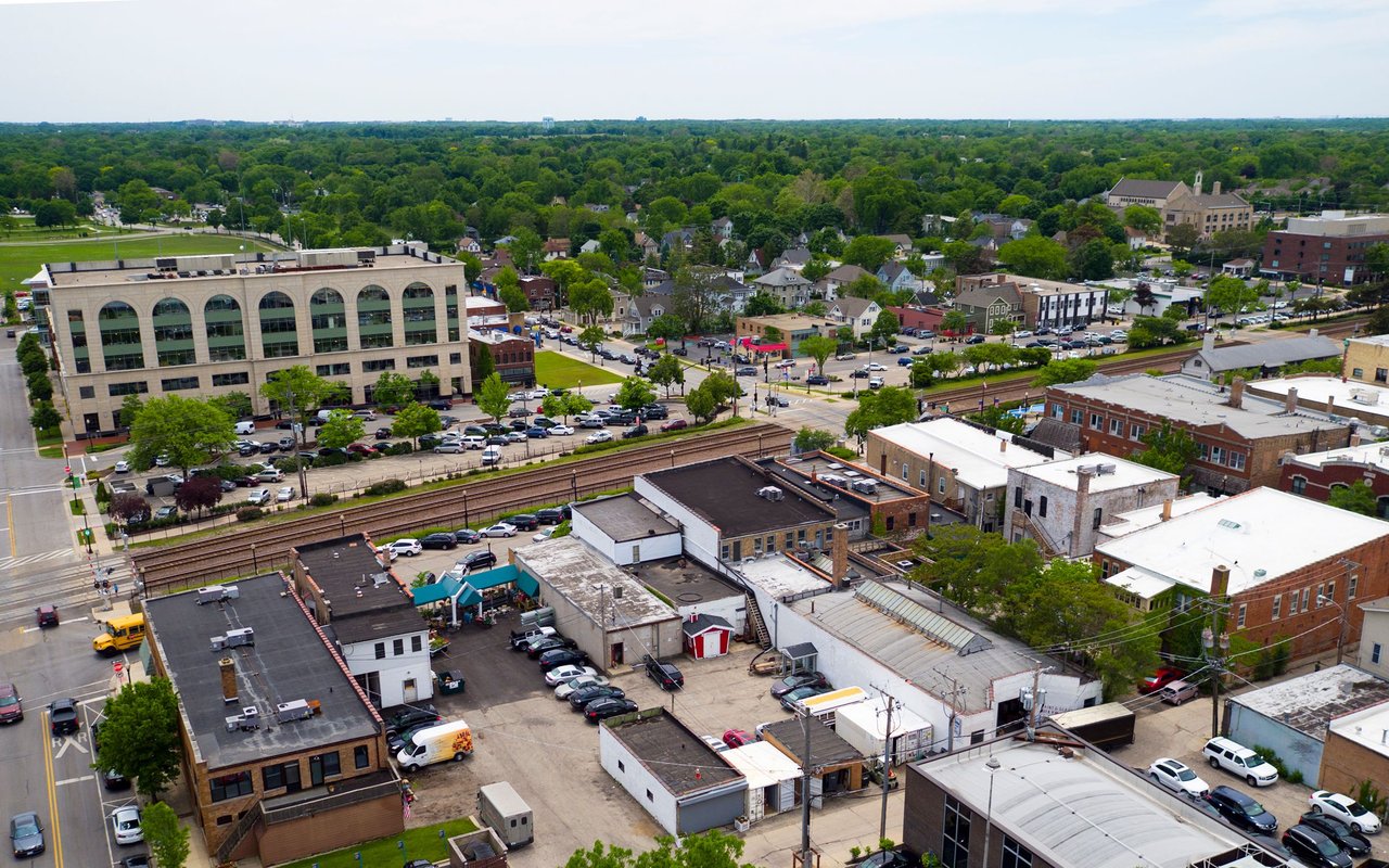 Aerial view of a leafy town center with railroad tracks and commercial buildings.