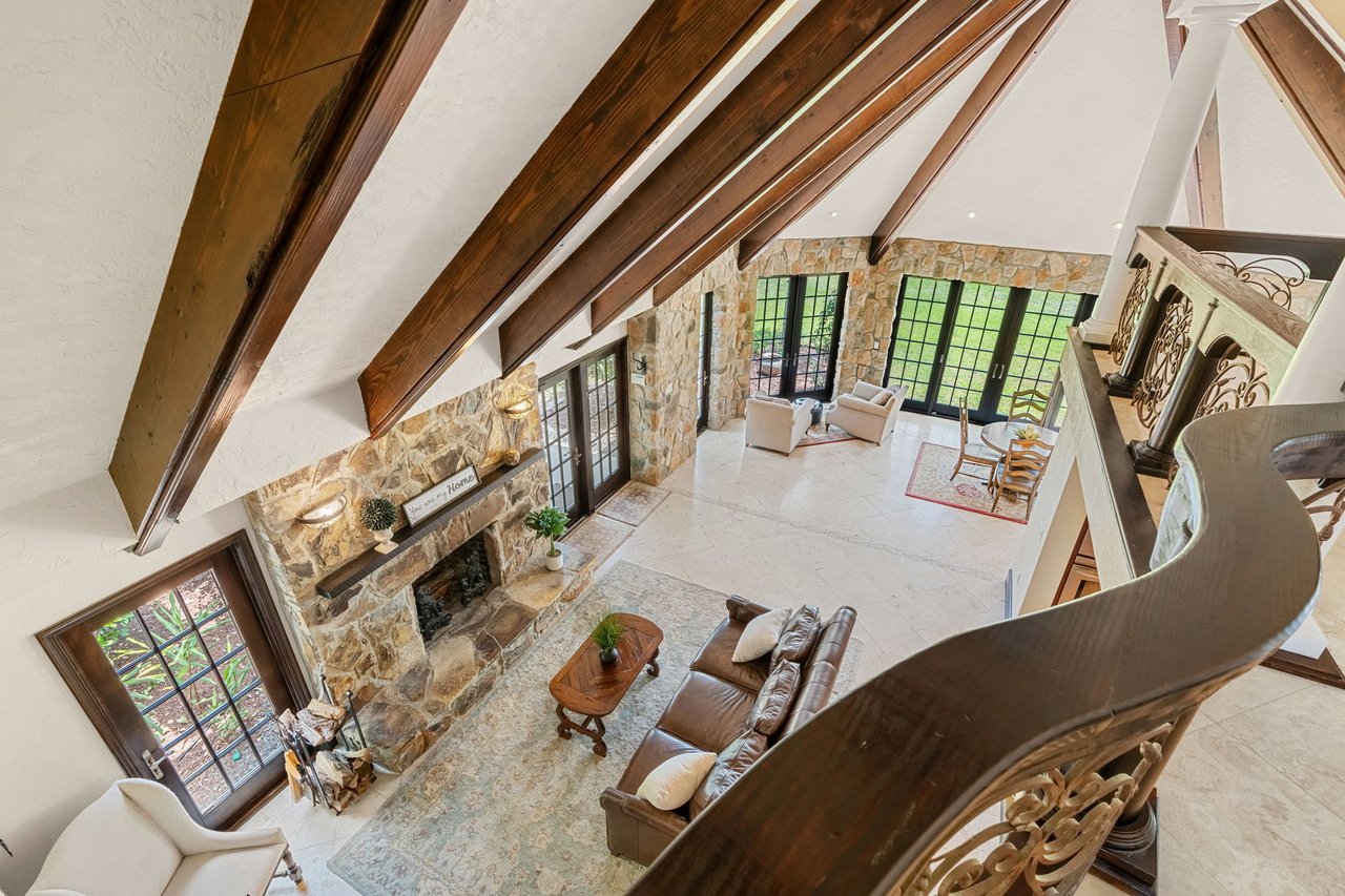 Living room with vaulted wood-beam ceilings, a stone fireplace, leather seating, and tall windows.