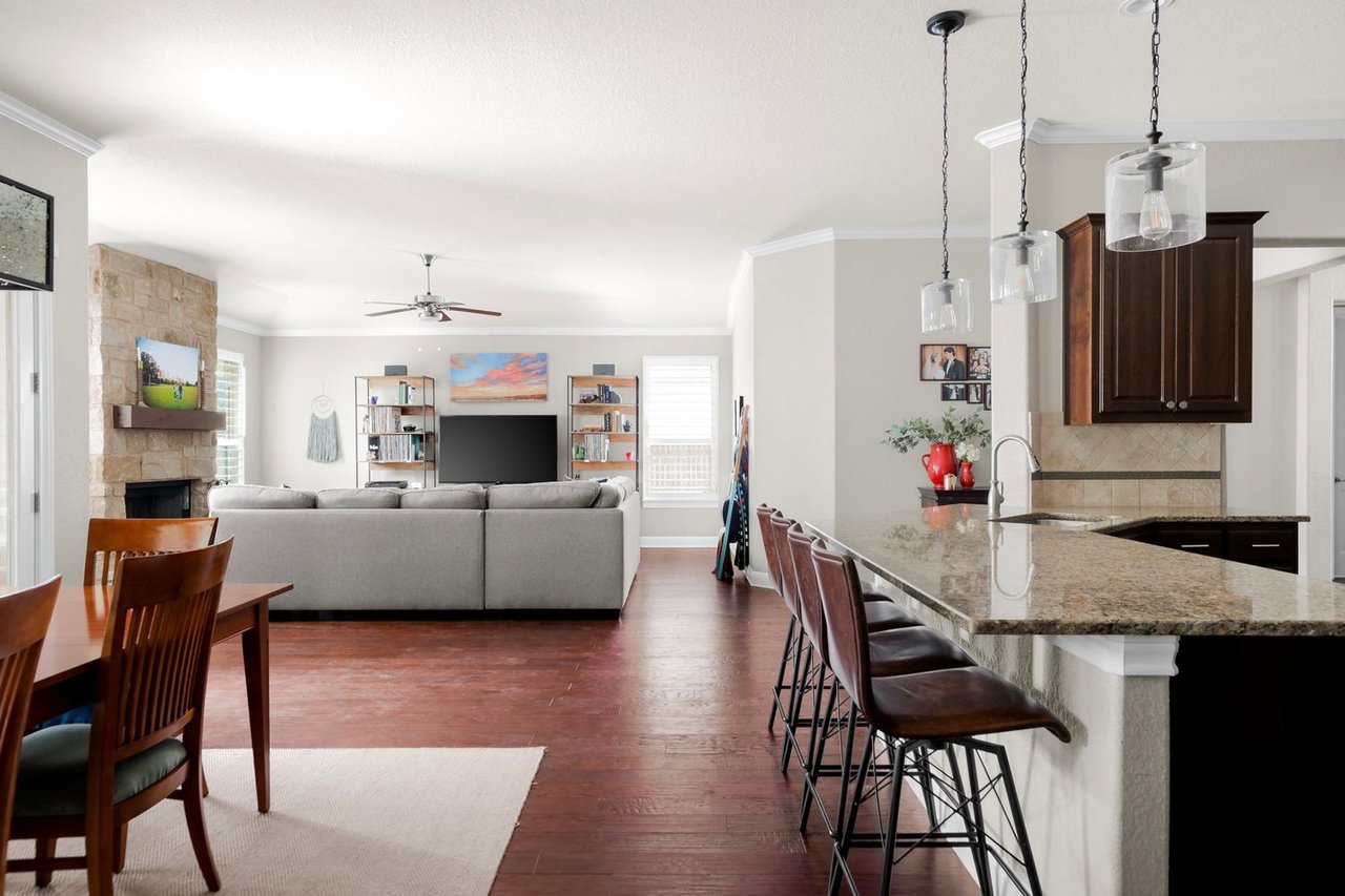 Open-plan living room and kitchen with a stone fireplace, granite island, and dark wood floors.