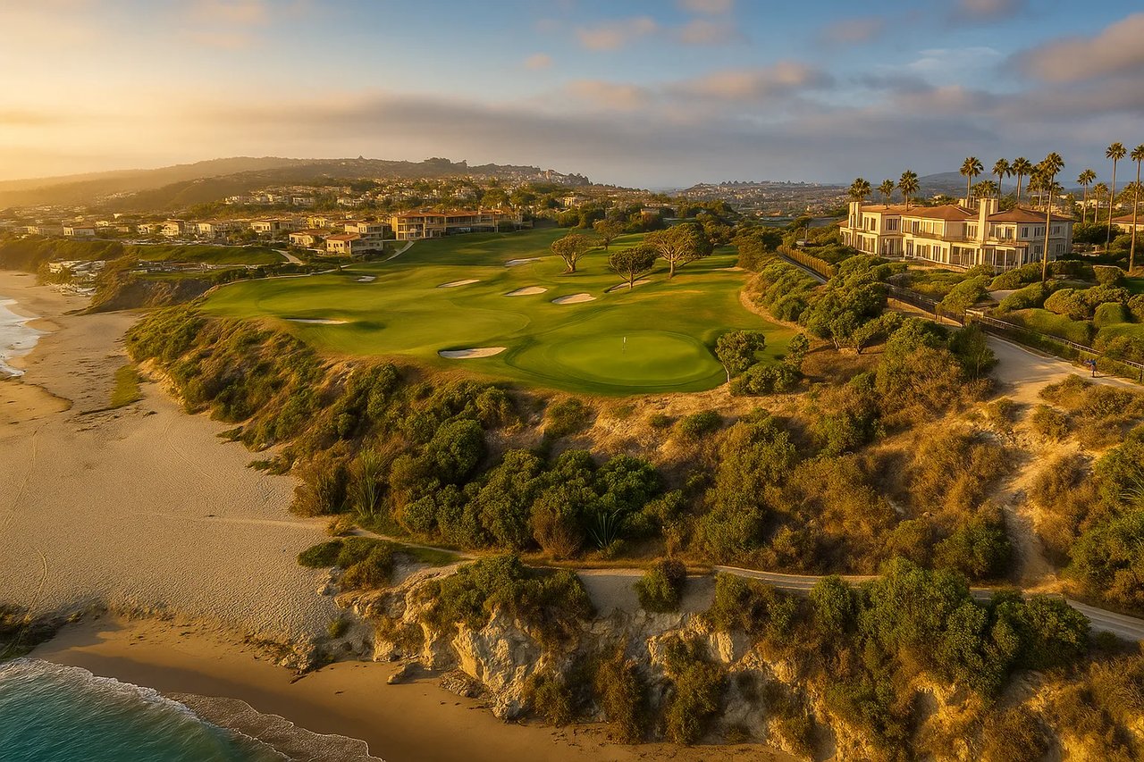Aerial view of Monarch Beach Golf Links in Dana Point, California, showing lush fairways along the coastline with luxury homes overlooking the Pacific Ocean at sunset.
