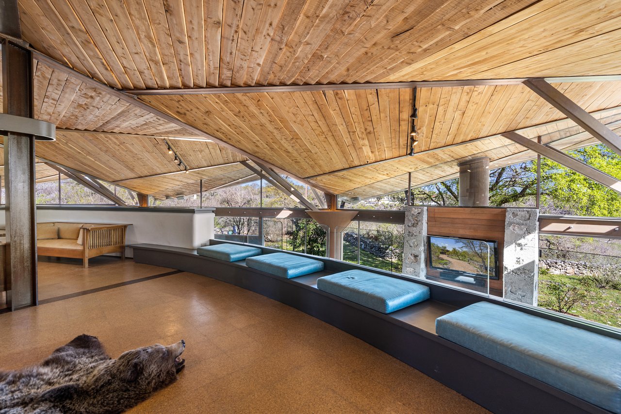 Media hall under a wood plank ceiling and exposed steel trusses, with a long built-in window bench facing the hill country, architect John Covert Watson, builder Don Crowell.