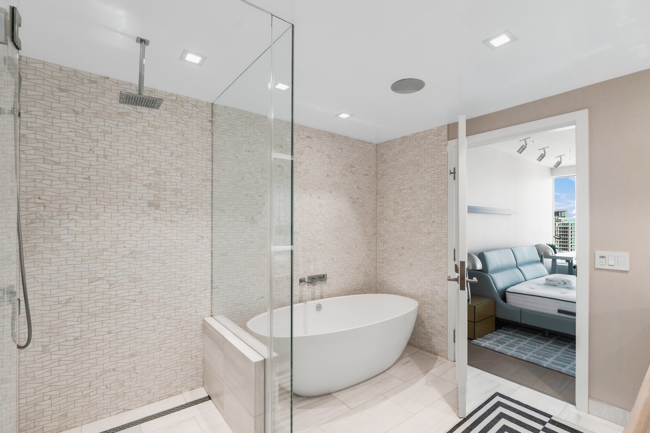 Modern bathroom with geometric tile, glass shower, and freestanding tub beside a bedroom.