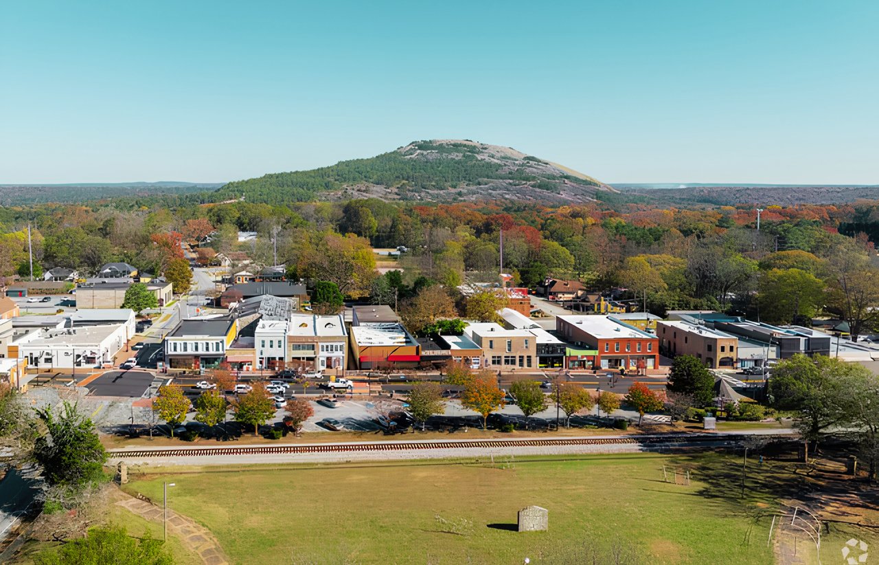 Aerial view of a small town and downtown buildings below a rocky, wooded mountain.