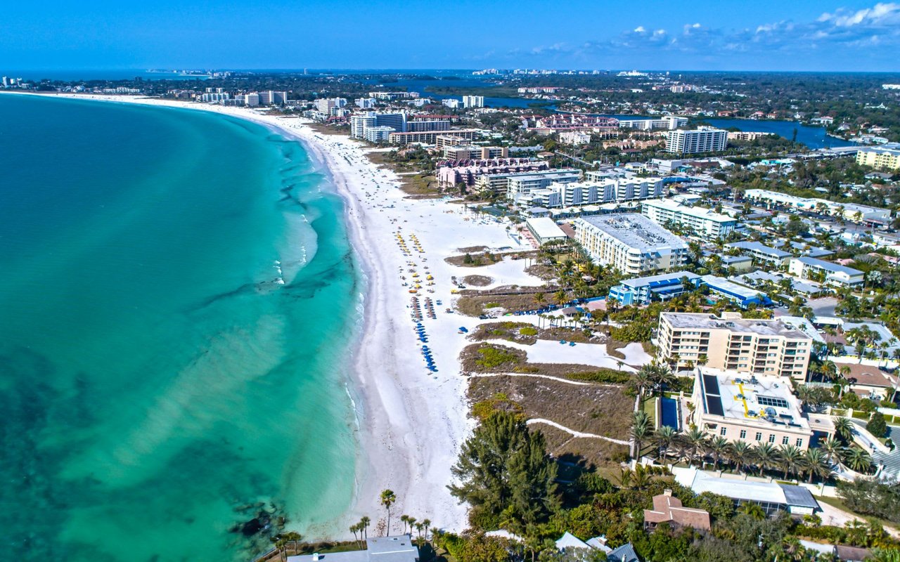 An aerial view of a beautiful beach with white sand and turquoise water surrounded by tall buildings.