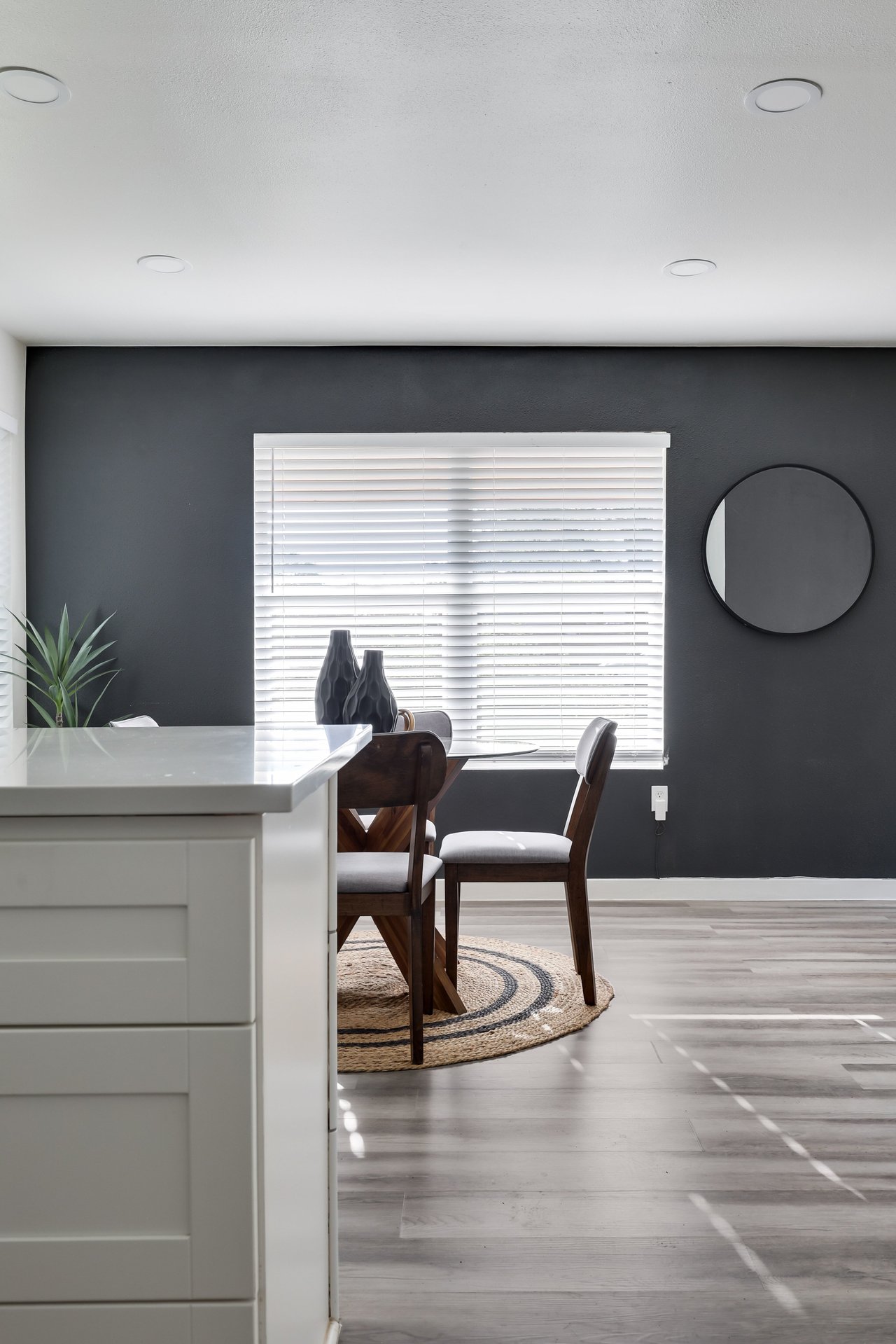 Dining area with dark wood chairs and a woven rug beside a white kitchen island.