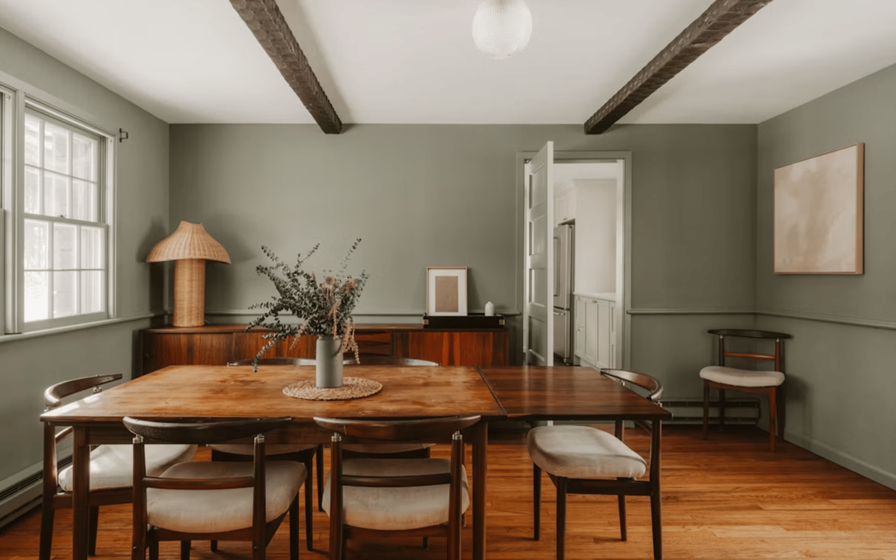 Furnished dining room with exposed ceiling beams, a large wooden table, and polished hardwood floors.