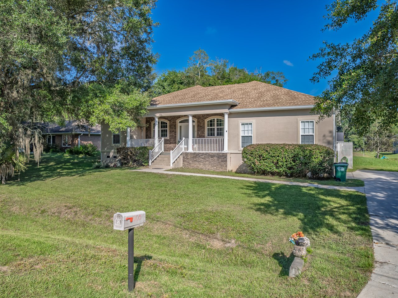 Single-story home with a broad covered porch, stone accents, and a large front lawn.