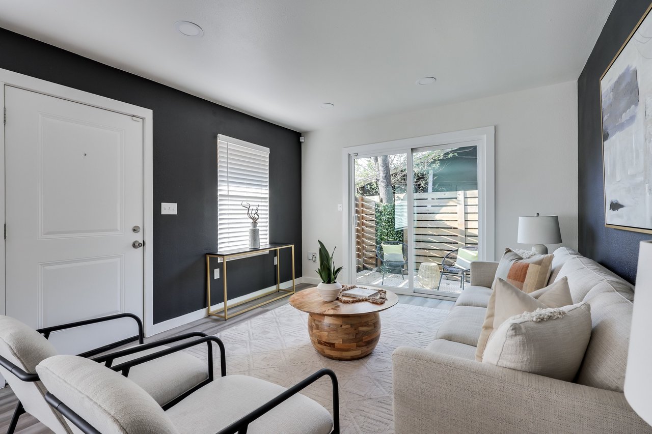 Furnished living room with a white sofa, round wooden coffee table, and sliding doors to a fenced patio.