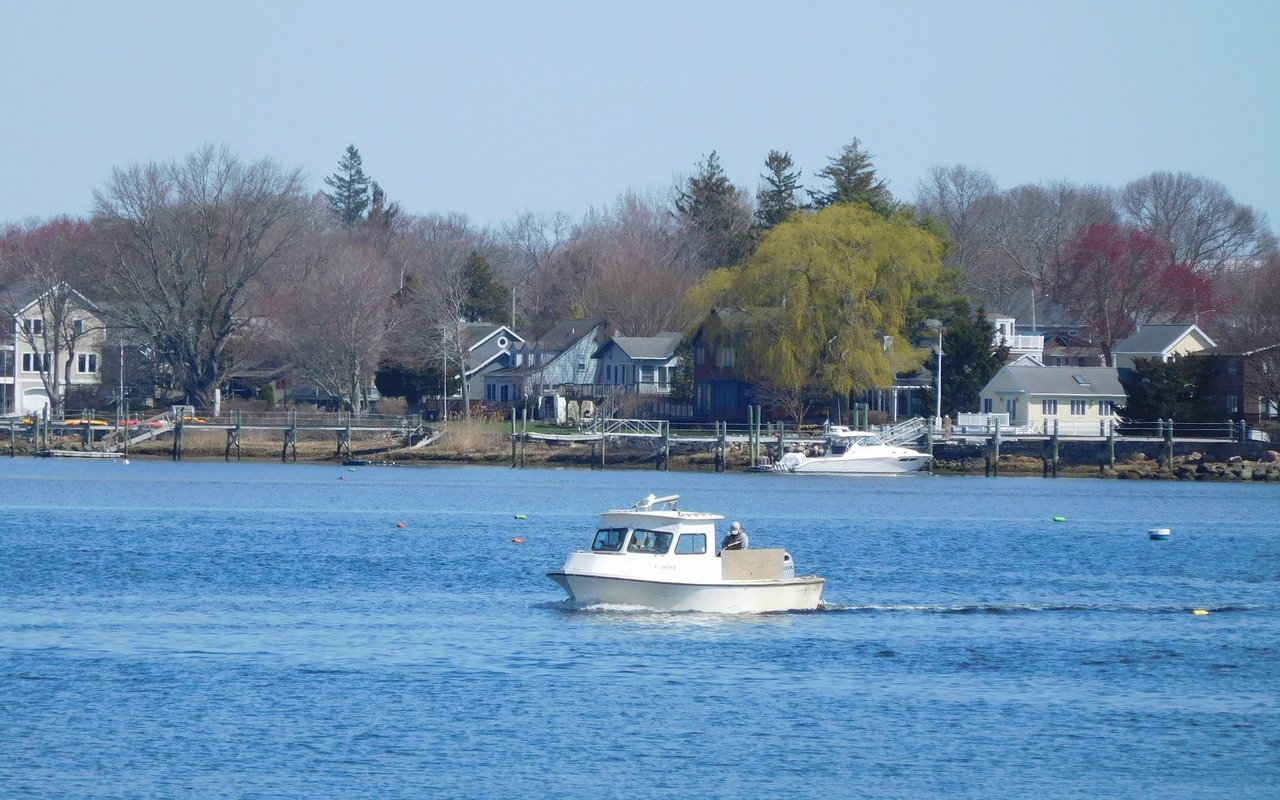Waterfront homes and docks line the shore as a small motorboat crosses the water.