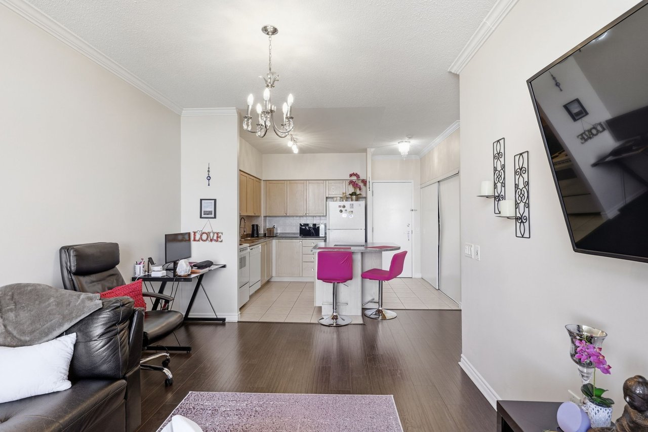 Open-plan condo living room and kitchen with a black leather sofa and two magenta island stools.