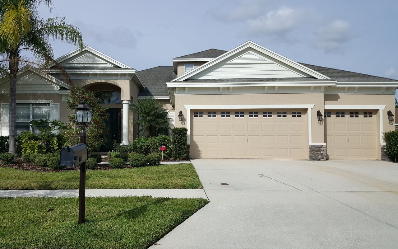Beige stucco home with three garage bays, a palm tree, and a wide driveway.