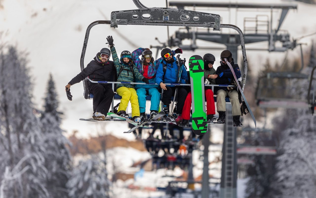Six skiers and snowboarders ride a chairlift, including one with a bright green snowboard.
