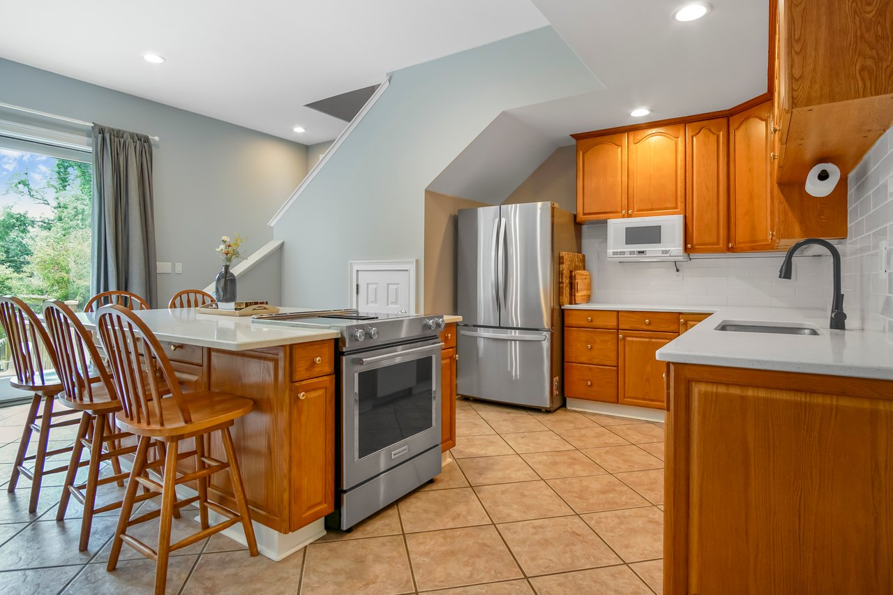 Modern kitchen with wooden cabinets, stainless steel appliances, and a large island with barstools. Neutral colors create a warm, inviting atmosphere.
