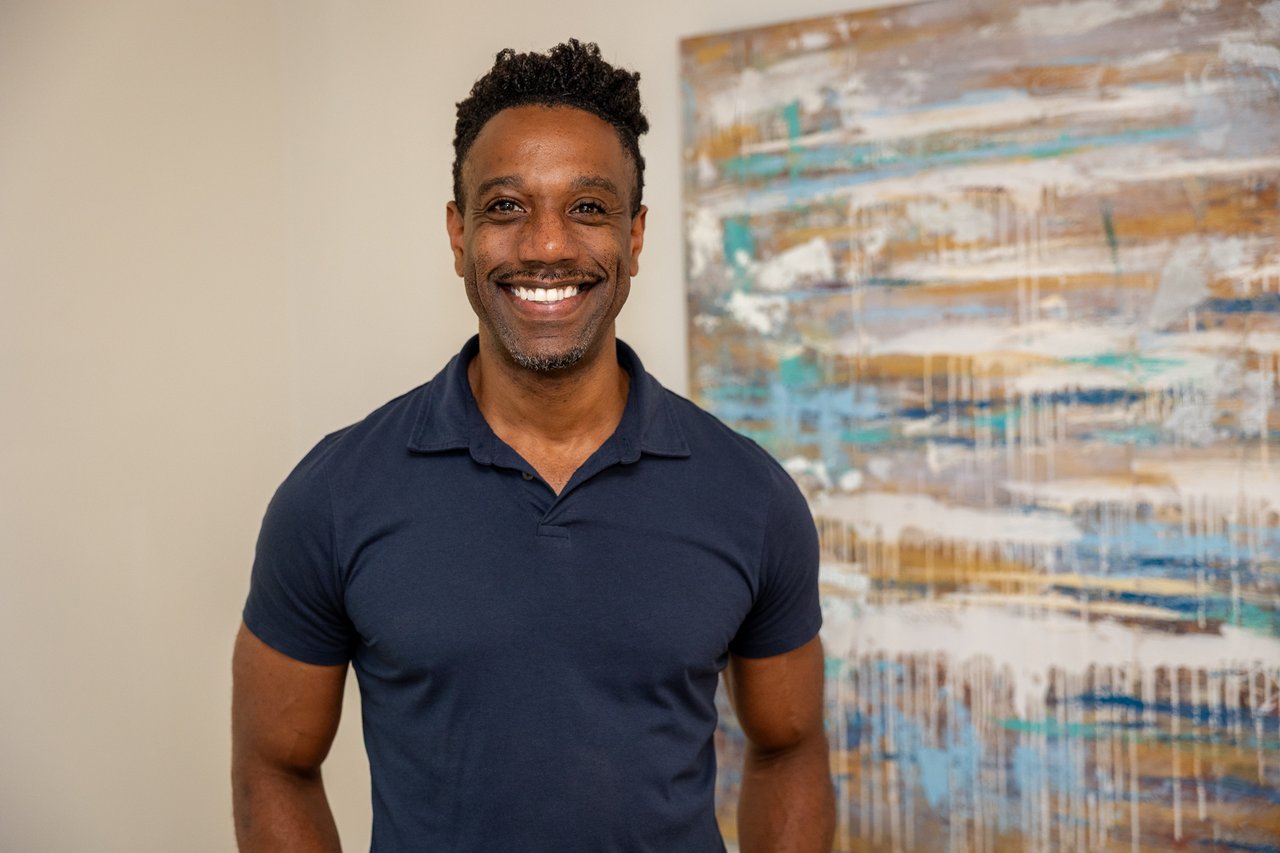 Smiling man in a navy polo standing in front of an abstract painting.