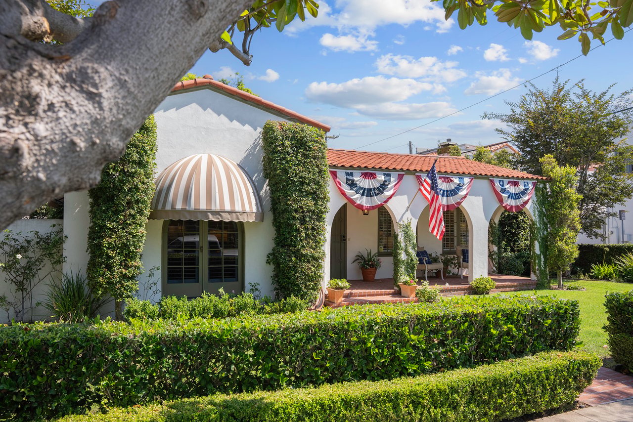 White stucco home with a red tile roof, arched porch, and patriotic bunting along the front.